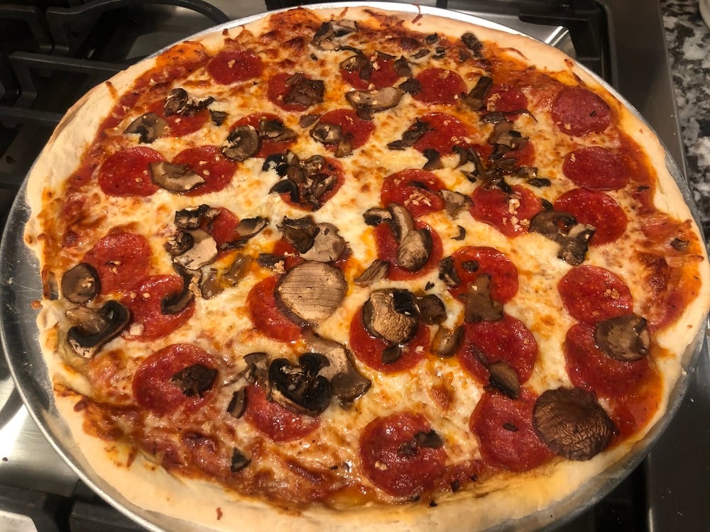 Chiếc bánh pizza New York tròn cỡ lớn, đế mỏng, nhân phủ phô mai vàng, nấm, xúc xích, thịt, sốt cà chua