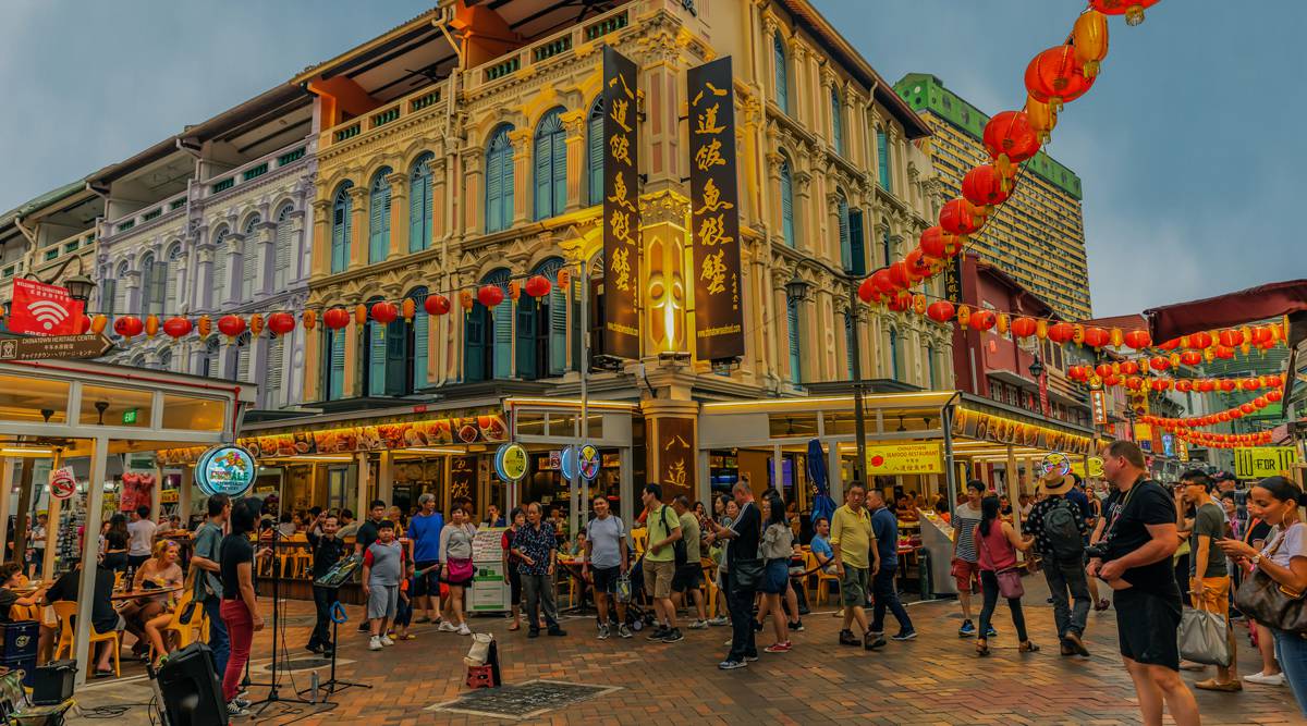 phố Chinatown có toà nhà trắng vàng, sạp hàng hoá, treo nhiều dây đèn lồng đỏ và nhiều người đi lại