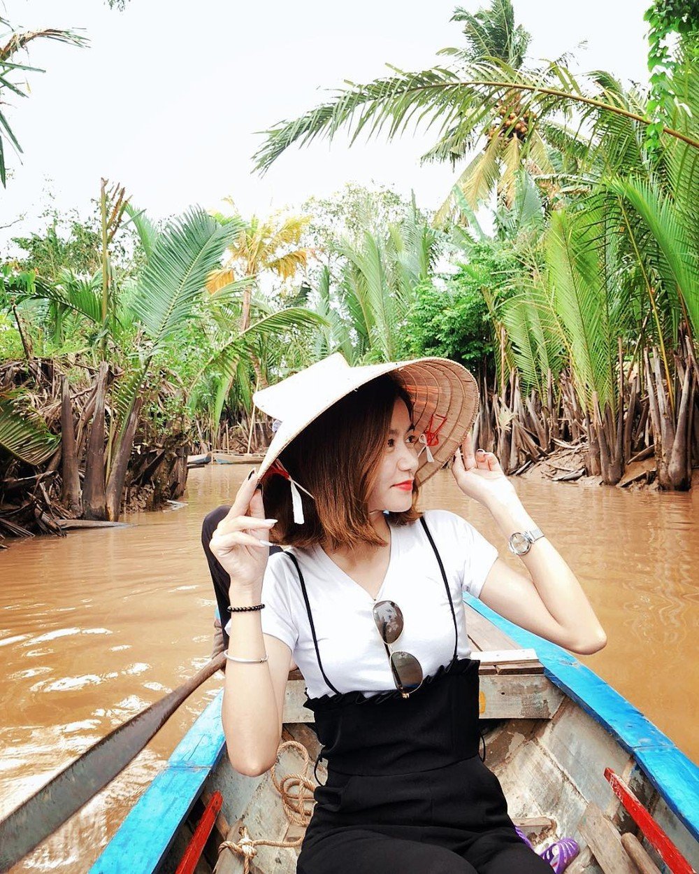 Bạn nữ đội nón chụp ảnh khi đang ngồi thuyền chạy dọc con sông ngắm miệt vườn xanh mướt