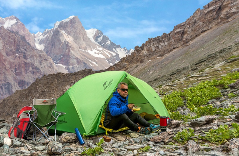 Người đàn ông ngồi trong lều màu xanh lá được dựng trên vách núi toàn sỏi đá