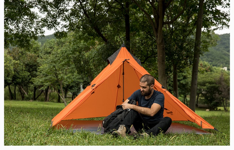 Người đàn ông đi cắm trại, dựng lều màu cam trên địa hình thảm cỏ xanh mướt