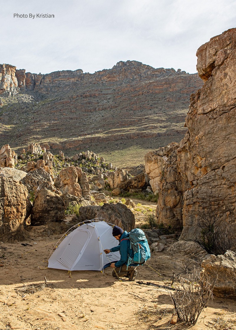 Người đàn ông đang dựng lều cắm trại trắng giữa những vách núi cao