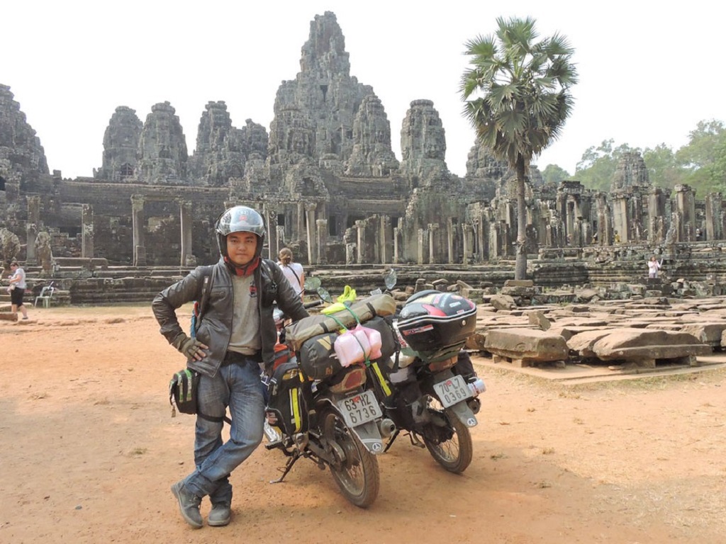 Một bạn nam người Việt dừng chân chụp ảnh bên cạnh chiếc xe máy phượt tại Campuchia