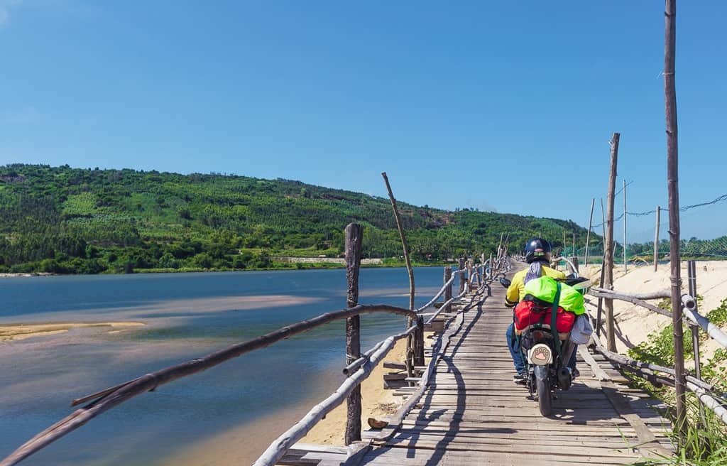Khách du lịch phượt Phú Yên bằng xe máy đang đi trên Cầu Gỗ Ông Cọp, xung quanh có biển xanh, đồi cây xanh