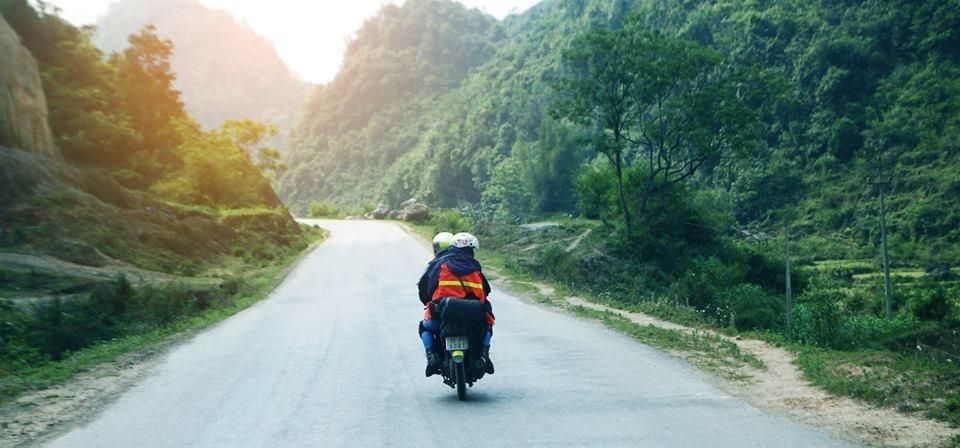 2 người du lịch phượt Sapa bằng xe máy, hai bên đường đi là đồi núi, rừng cây xanh