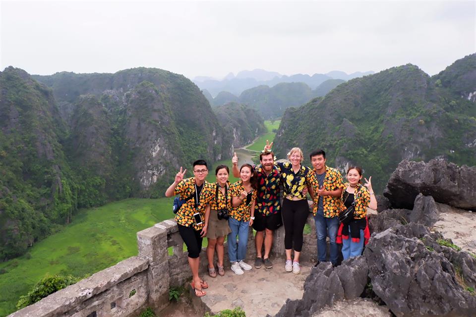 Một đoàn du khách mặc những bộ đồ năng động: áo phông, sơ mi, quần lửng... chụp ảnh tại khu du lịch Ninh Bình