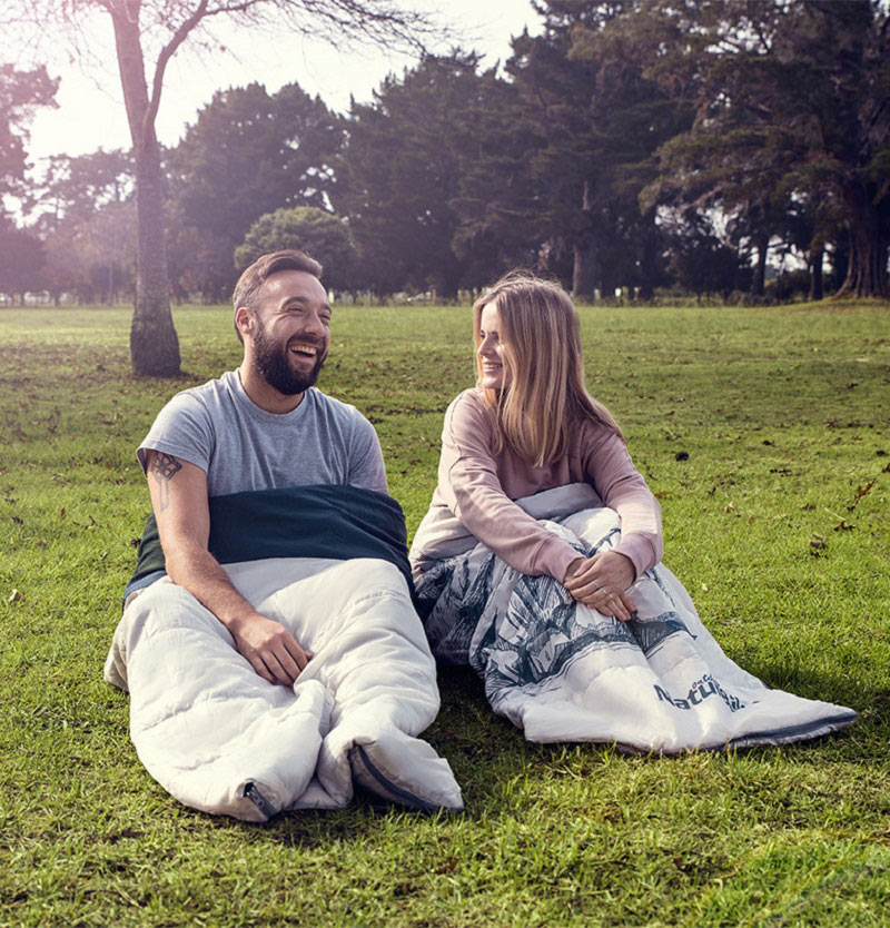 Bạn nam và bạn nữ tách túi ngủ đôi thành 2 túi ngủ và ngồi trò chuyện vui vẻ trên nền cỏ xanh