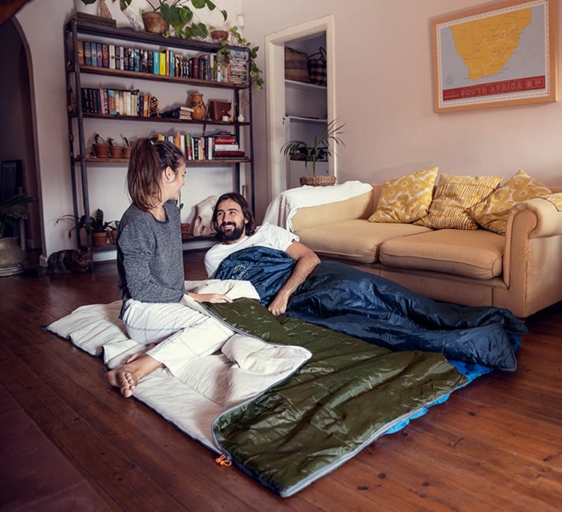 Cặp vợ chồng trải túi ngủ nằm thư giãn trên nền nhà phòng khách