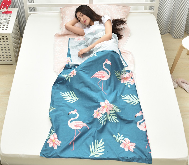 Bạn nữ sử dụng túi ngủ màu xanh hoạ tiết cò, hoa ở trên giường