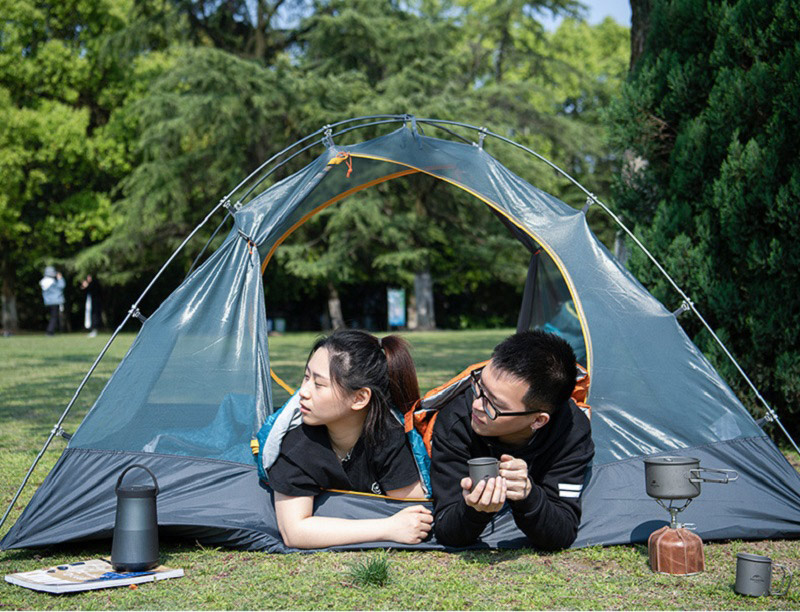 Bạn nam và nữ cùng nằm sấp trong túi ngủ trải ở trong lều cắm trại, nhìn ra ngoài trời ngắm cảnh