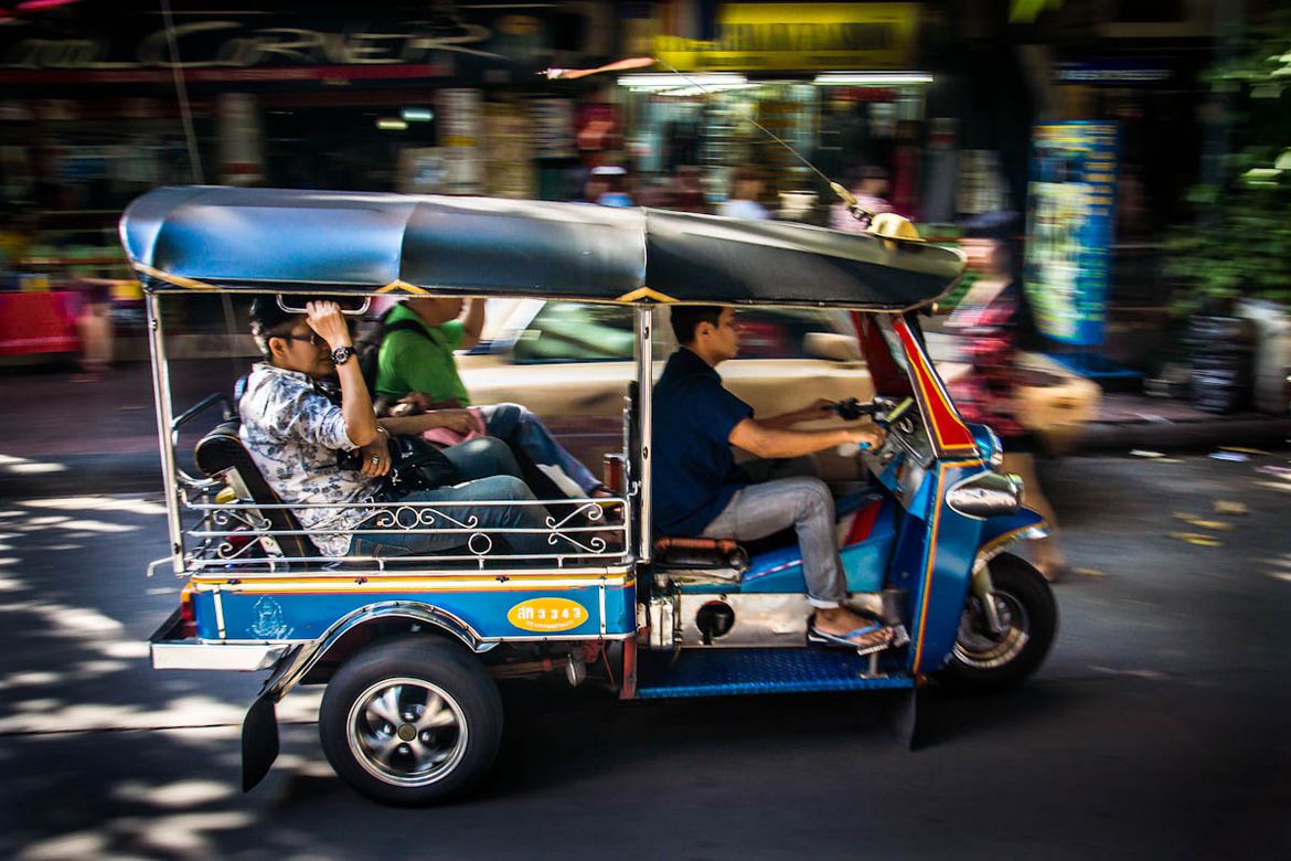 Một chiếc xe tuk tuk màu xanh có 3 người ngồi đang đi trên đường Campuchia