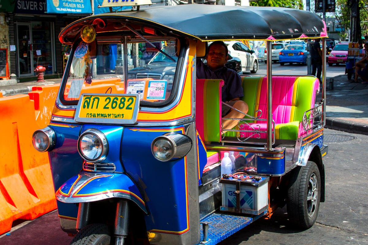 Một người đàn ông ngồi trong xe tuk tuk nhiều màu sắc có mái che ở Thái Lan