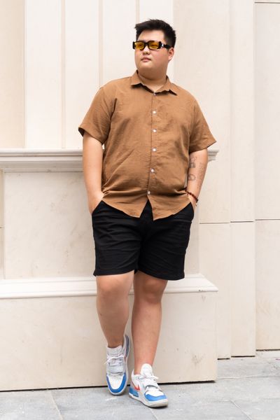 Người mẫu nam ngoại cỡ mặc áo sơ mi đũi màu nâu big size kết hợp vơi quần short kaki đen
