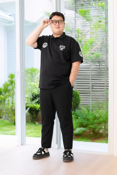 Người mẫu nam mặc set đồ big size: Áo polo đen theo logo và quần âu đen và sneaker