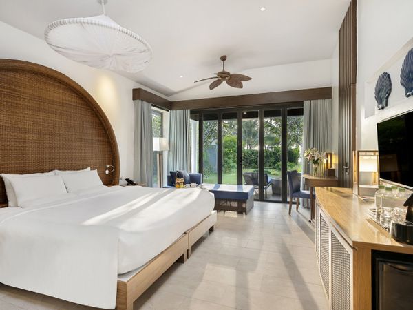 phòng resort novotelcó giường, cửa ban công rộng, bàn ghế và tivi