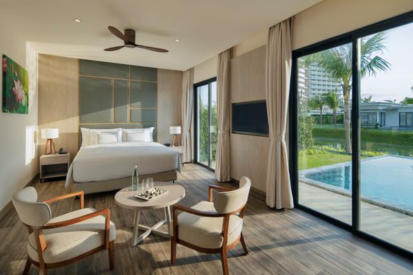 căn phòng có giường đôi, bàn ghế, sàn lót gỗ, và cửa lớn view ra biển