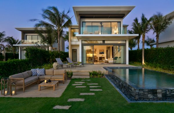 biệt thự 2 tầng có đèn vàng, phía trước có hồ bơi và bộ bàn ghế