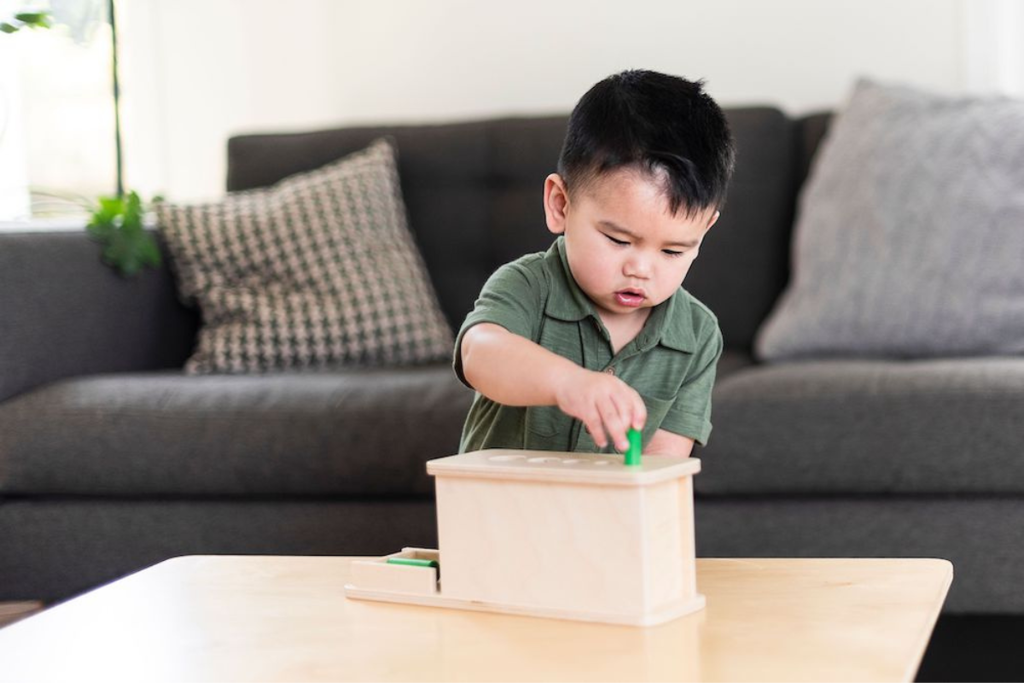 Hình ảnh trẻ chơi sản phẩm đồ chơi Montessori Hình trụ rơi trong Hộp đồ chơi Thử Thách của Kinderlove cho các bé 20-21 tháng tuổi
