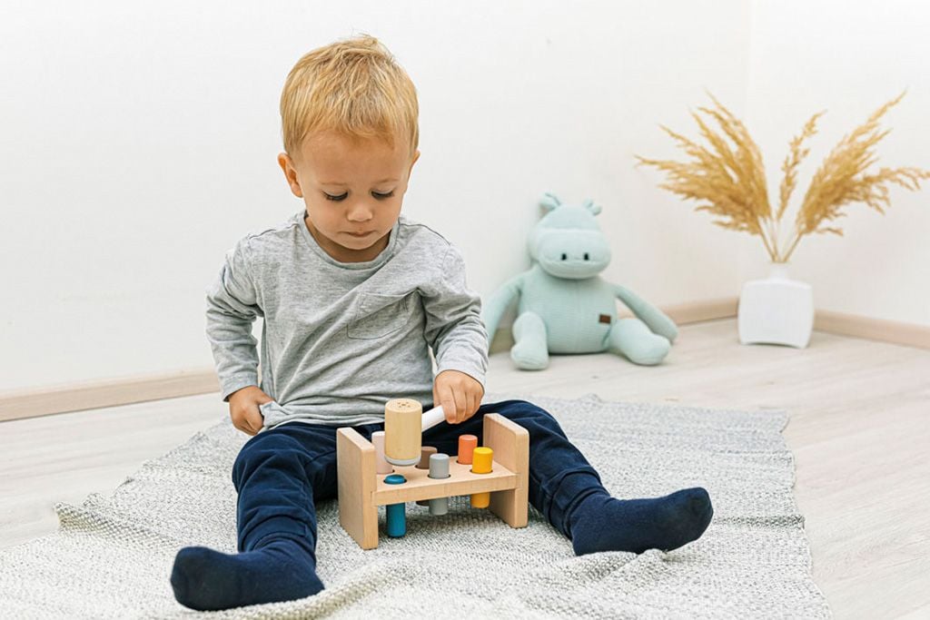 Hình ảnh trẻ chơi đồ chơi Đập búa lên cọc gỗ trong hộp đồ chơi Suy Nghĩ của Kinderlove cho trẻ 10-11 tháng tuổi