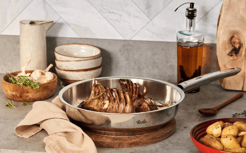 Chảo inox Fissler sáng bóng đang áp chảo một miếng sườn với lớp vỏ ngoài vàng nâu hấp dẫn.