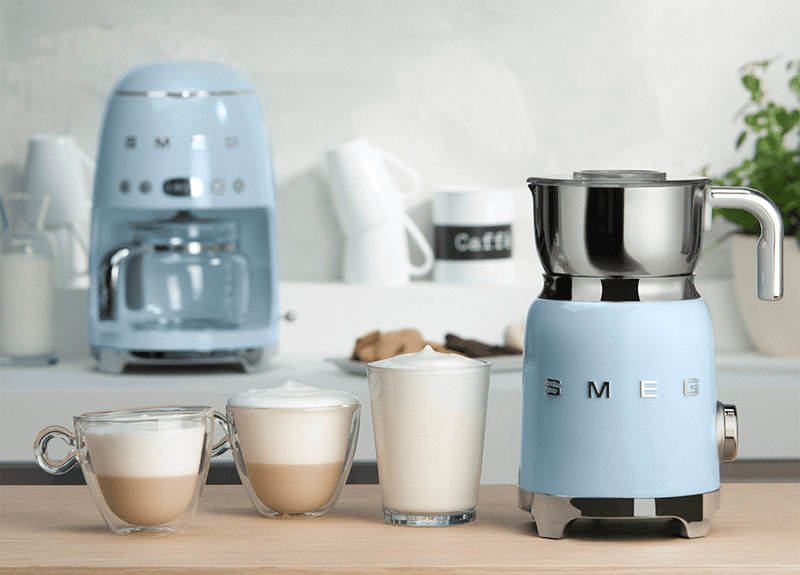 Máy đánh bọt sữa SMEG nhỏ gọn kiểu dáng cổ điển Ý bên cạnh tách cà phê cappuccino