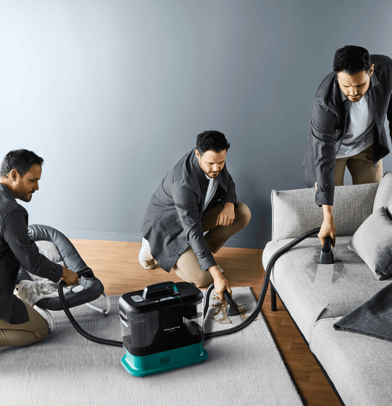 Một người đang dùng máy giặt thảm cầm tay Rowenta để làm sạch vết bẩn trên một tấm thảm màu kem