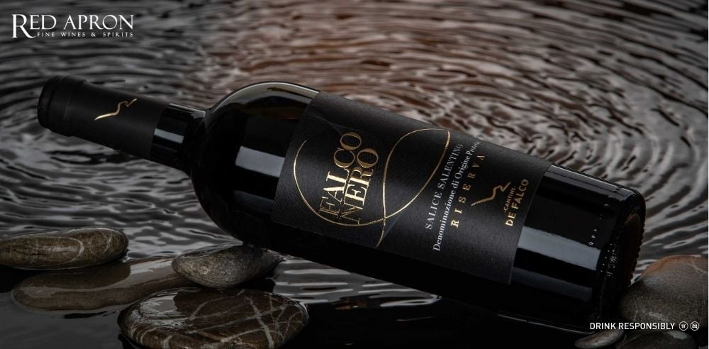 Rượu vang FALCO NERO Salice Riserva DOP, Negroamaro pha Malvasia Nera, chai rượu đặt trên nền gỗ tối.
