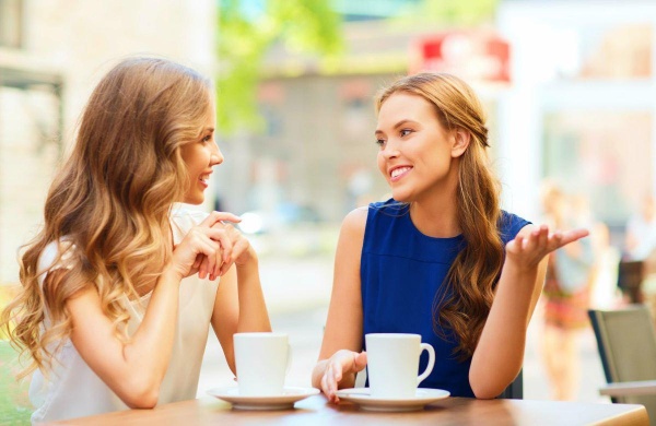 Không nên uống quá nhiều cà phê có chứa caffeine để giảm thiểu rủi ro sức khỏe. Hai người phụ nữ đang tán gẫu với hai ly cà phê được đặt trên bàn